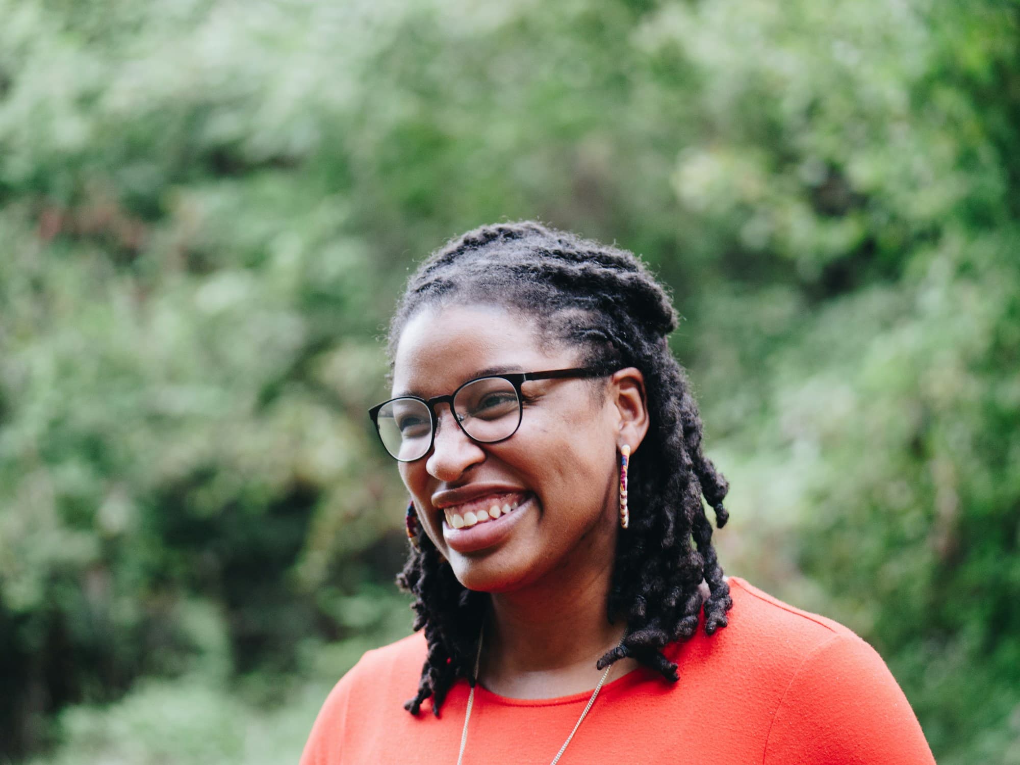 A woman with locs and glasses, smiling, outdoors